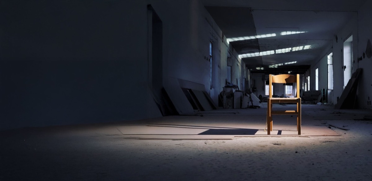 A wooden chair at the center of an empty industrial hall at the Lanificio, lit by daylight falling through the skylights.